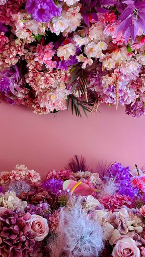 A vibrant floral arrangement with pink and purple flowers against a soft pink background, showcasing a variety of textures and colors.