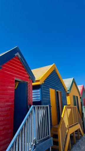 Vibrant beach huts in red, blue, and yellow under a clear blue sky at Muizenberg Beach, Cape Town, South Africa.