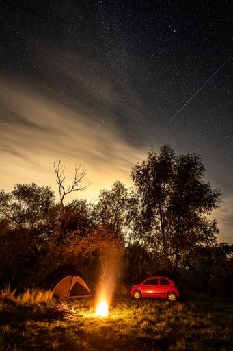 A vertical shot of a bonfire in the forest next to a tent and a car