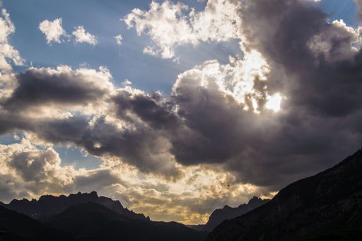 Dramatic mountain landscape with sun rays breaking through clouds over rugged peaks at sunset.