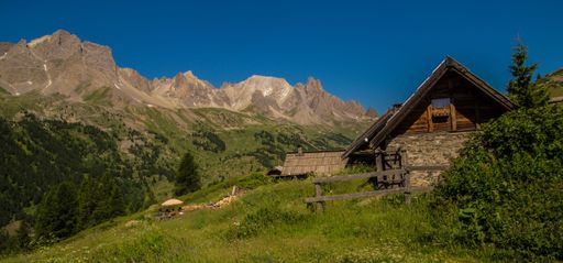 Rustic mountain cabin with lush green landscape and majestic peaks under a clear blue sky in the French Alps.