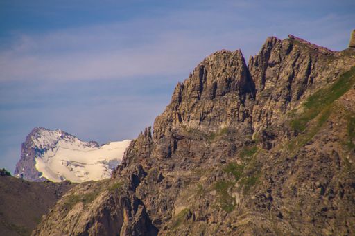 A majestic mountain range with rugged peaks and a distant snow-capped summit under a clear blue sky.
