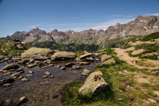 Scenic mountain landscape with rocky terrain and a clear blue sky, featuring a small stream in the foreground.