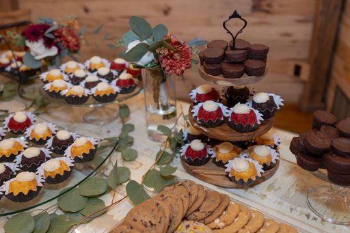 An elegant dessert table with assorted bundt cakes, cookies, and floral decor, perfect for a rustic wedding or event.