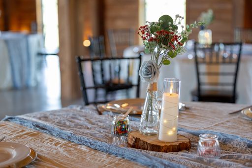 An elegant wedding table setting with a candle and floral centerpiece on a rustic wooden table in a cozy venue.