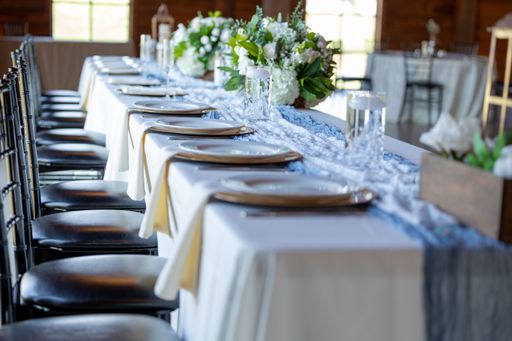 An elegant banquet table setting with white linens, plates, and floral centerpiece in a rustic venue.