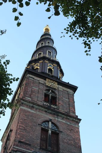 A towering historic church spire framed by trees against a clear sky, in the Nyhavn area, Copenhagen.