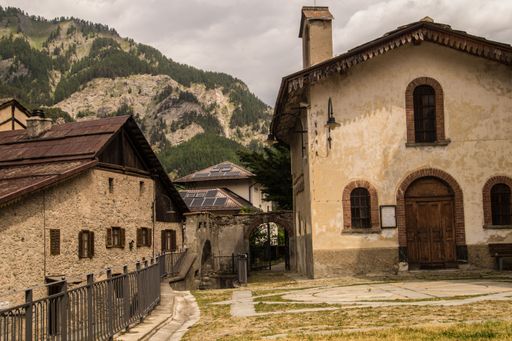 Charming rustic buildings in a mountain village with lush green hills in the background under a cloudy sky.