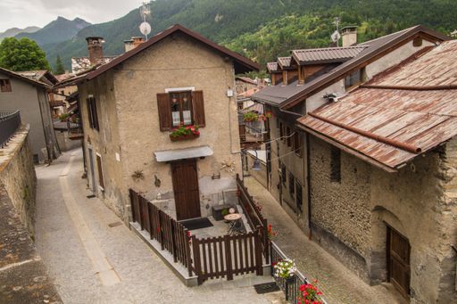 Charming alpine village street with rustic stone houses and vibrant flowers, nestled in a lush mountain landscape.