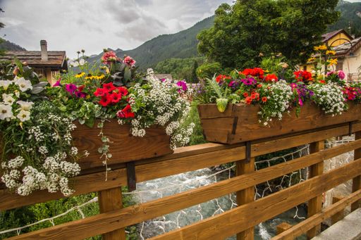 Colorful flowers in wooden planters on a rustic bridge with a mountainous backdrop under a cloudy sky.