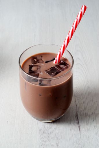 A efreshing glass of iced chocolate milk with a red striped straw on a light wooden table.