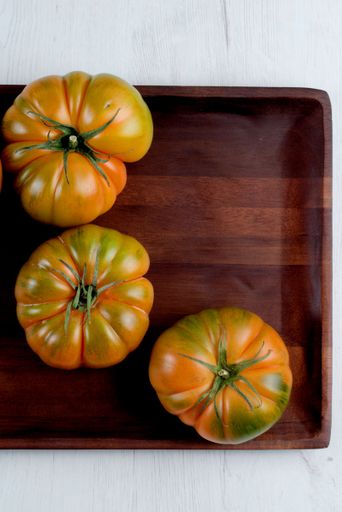 Three heirloom tomatoes on a wooden tray over a white background, showcasing vibrant colors and natural textures.
