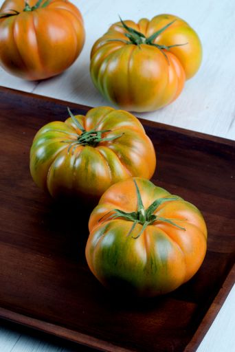A close-up of ripe heirloom tomatoes on a wooden tray with a white background, showcasing vibrant colors and texture.