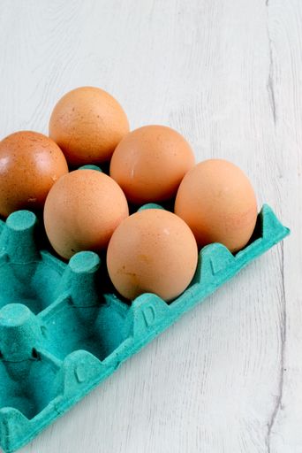 Fresh brown eggs in a blue carton on a light wooden surface, perfect for culinary themes.