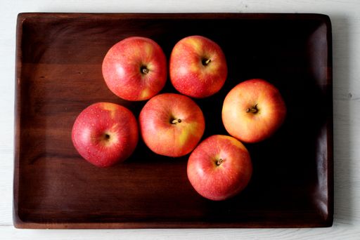 A top view of six red apples arranged neatly on a wooden tray, set against a light wooden background.