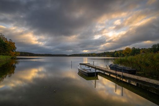 An atmospheric landscape at the verge of sunset. Heavy clouds cast a dramatic glow over the quiet, reflective expanse.