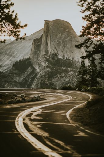 A vertical shot of a road near a mountain surrounded by trees