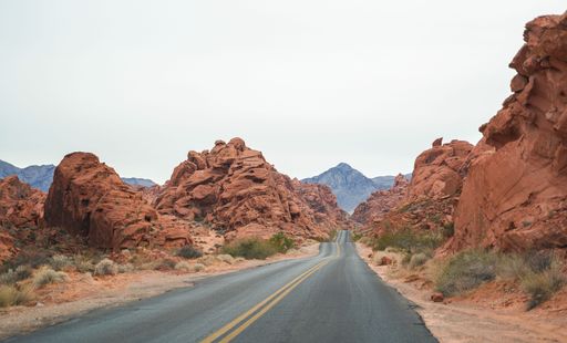 A scenic road through red rock formations in Valley of Fire State Park, Nevada, under a cloudy sky.