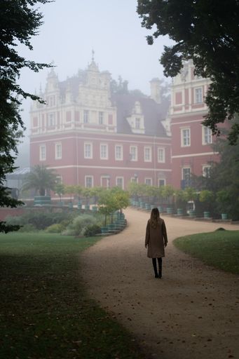 A vertical shot of a woman walking towards the Schloss Muskau in Saxony, Germany on a foggy morning