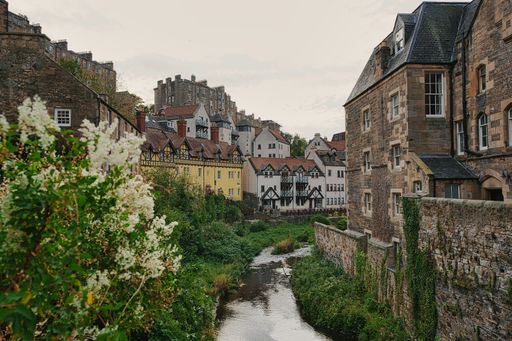 Charming view of Dean Village in Edinburgh, Scotland, featuring historic buildings and a tranquil stream surrounded by lush greenery.