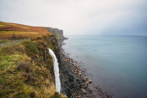 Scenic view of Kilt Rock and Mealt Falls on the Isle of Skye, Scotland, with dramatic cliffs and a tranquil sea under a cloudy sky.