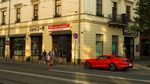 Tourists looking at a red Mustang sports car parked on a central street in Krakow, Poland.
