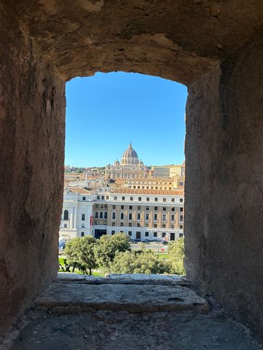 View of St. Peter's Basilica framed by a stone window in Rome, Italy, under a clear blue sky.