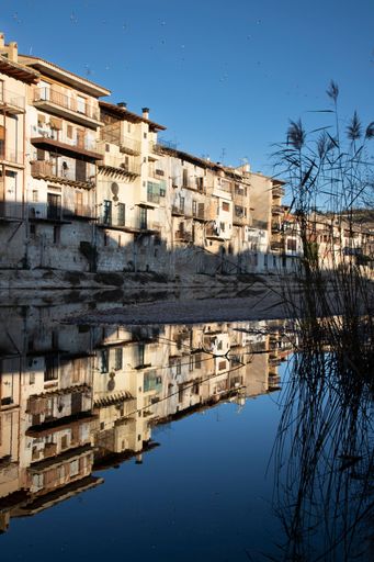Rustic buildings reflecting in a calm river in Valderrobres, Spain, under a clear blue sky