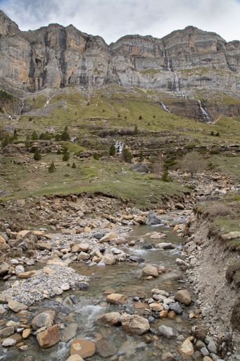 Scenic view of rocky mountain landscape with waterfalls and stream under cloudy sky in Pradera de Ordesa, Spain