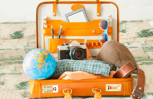 A close-up shot of a vintage camera, the globe, glasses, and an open suitcase full of other travel items.