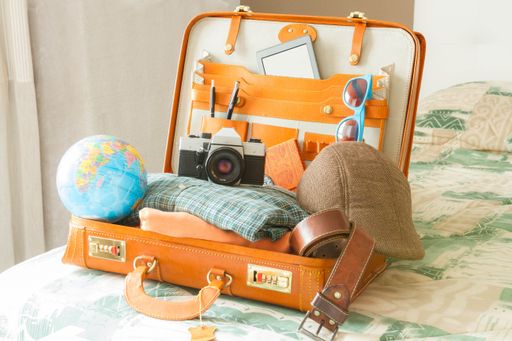 A close-up shot of a vintage camera, the globe, glasses, and an open suitcase full of other travel items.