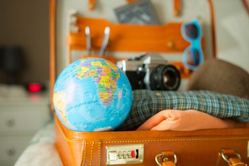 A close-up shot of a vintage camera, the globe, glasses, and an open suitcase full of other travel items.