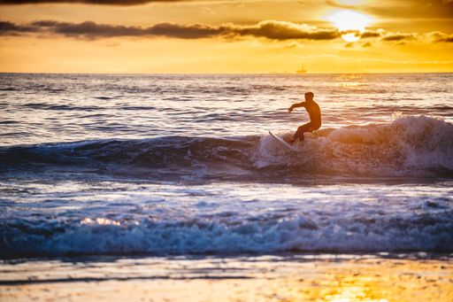 A shot of Caucasian male surfing the ocean waves with the background of yellow sunset