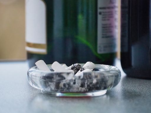 A closeup shot of a glass ashtray with ash and cigarette butts on the table