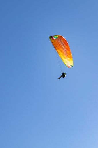 A vertical shot of a paraglider flying on a colorful parachute against a clear blue sky
