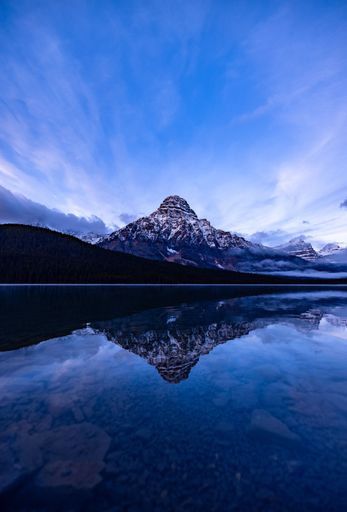 A stunning reflection of a snow-capped mountain in a tranquil lake under a vibrant blue sky at sunrise.