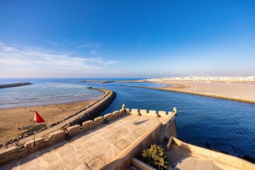 Scenic view of the Rabat beach and fortress under a clear blue sky, featuring sandy shores and ocean waters in Morocco.