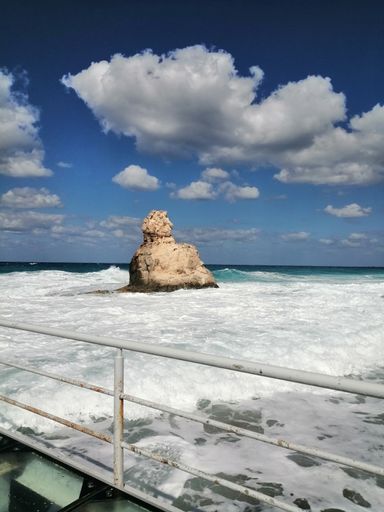 A vertical shot of a rock in a sea under the cloudy skies