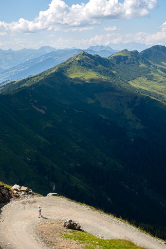 A vertical shot of a girl walking down the side of a mountain while looking at her phone