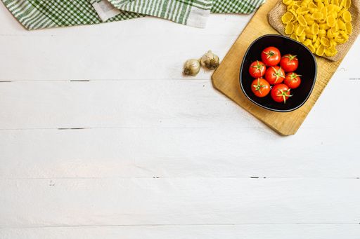 The pasta, cherry tomatoes , garlic, and chopping board on a wooden table with free space for text