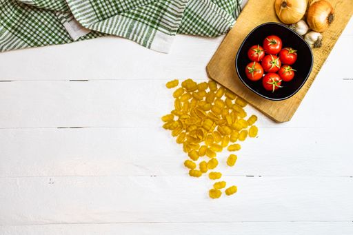 The pasta, cherry tomatoes , garlic, and chopping board on a wooden table with free space for text