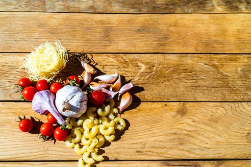 The fresh cherry tomatoes, garlic, and pasta on wooden table-  Italian food ingredients concept