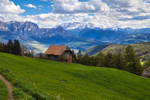 A high angle of a hut on a green hill with the background of forests and snowy mountains in a cloudy weather