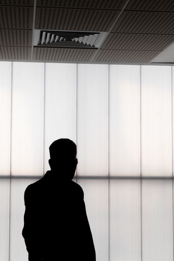 A vertical shot of a male's silhouette standing in front of a grey wall
