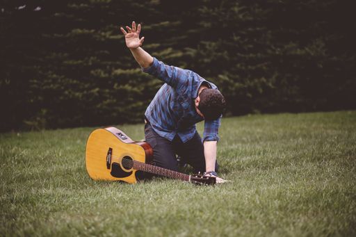 A selective focus shot of an emotional male outside with his guitar
