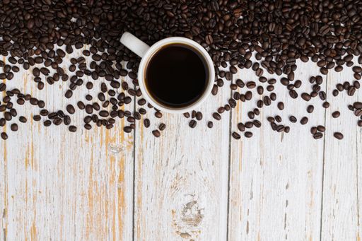 A top view of coffee beans and a cup of coffee on the upper side of a wooden desk with a copyspace