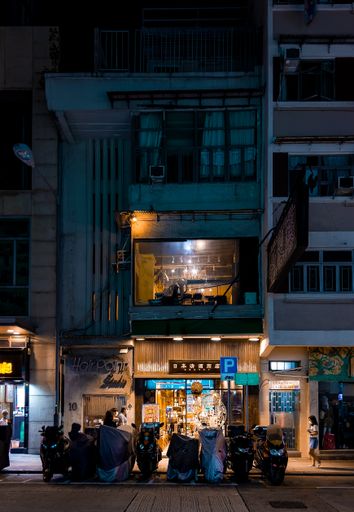 A vertical shot of a street with parked scooters and illuminated store at night. Kowloon, Hong Kong.