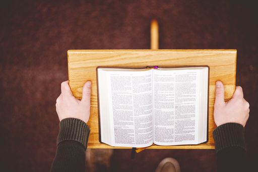 A closeup shot of a wooden speech stand with an opened book and person hands holding it