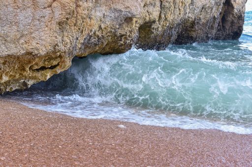 A closeup shot of the waves of the ocean under the cliff