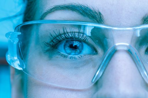 A close up view on the eyes of a pretty young Caucasian with lab glasses. Blue athmosphere